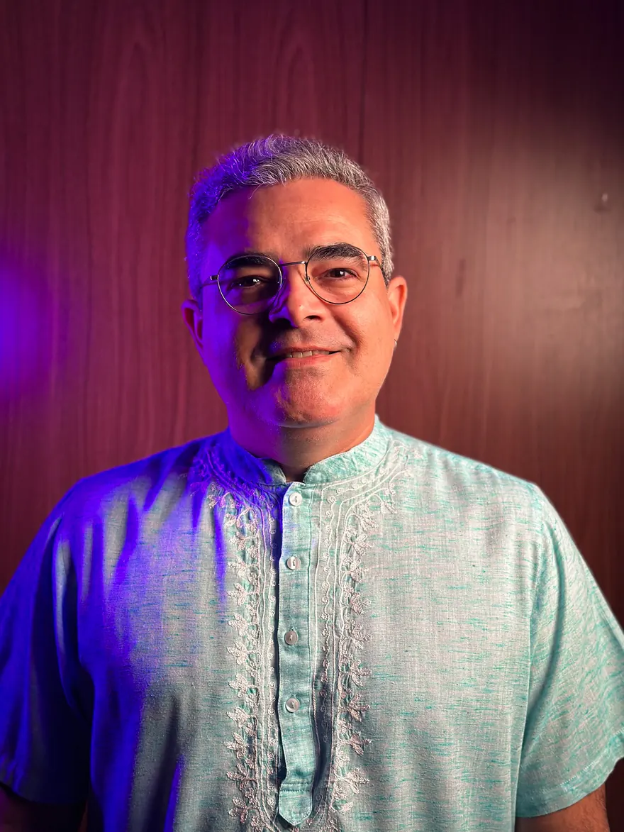 Sidnei Bonfim, criador do Método CÉU, sorrindo, de camisa azul-turquesa bordada, sob uma luz violeta